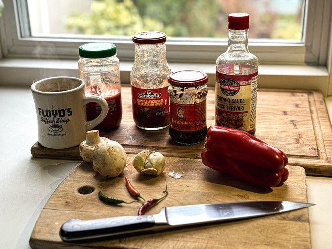 Photo of bottled sauces and a cutting board with peppers and garlic.