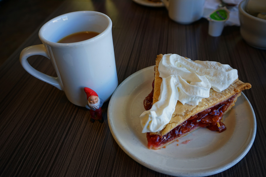 photo of cherry pie and coffe with a little garden gnome next to it.