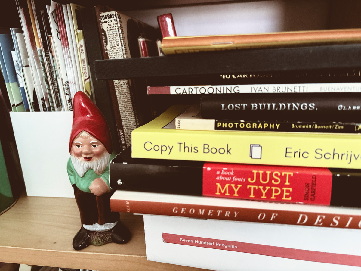 Image of a bookshelf with reading material next to a garden gnome.