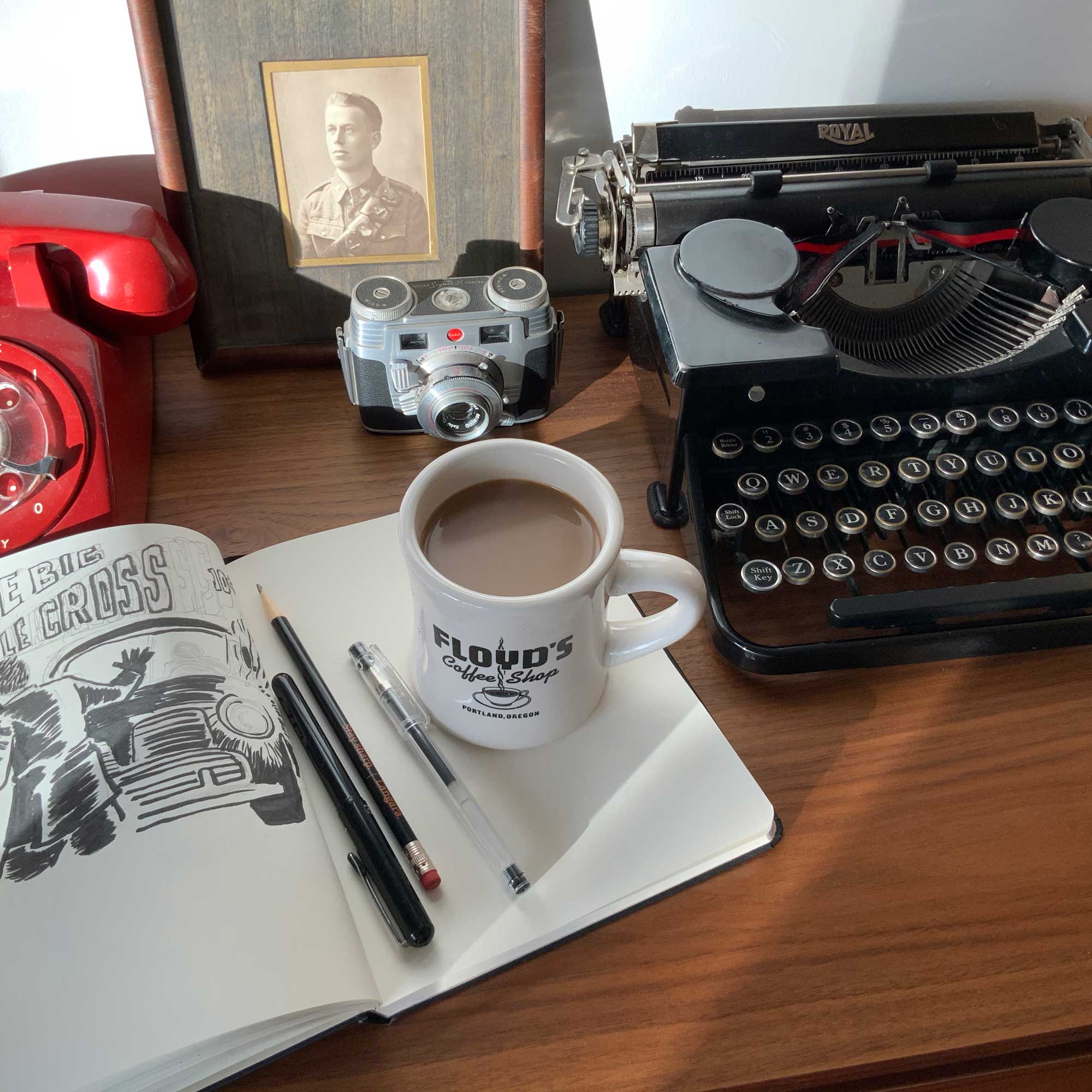 Photo fo sketchbook, a coffee cup, old camera and an old Royal typewriter.