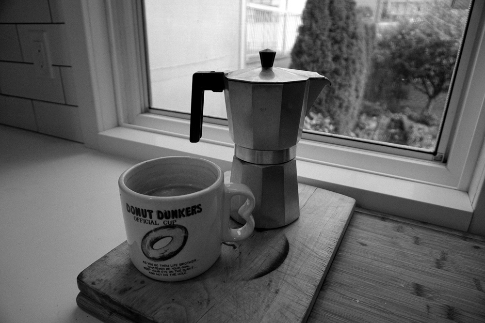 Coffee cup and coffee maker by window.